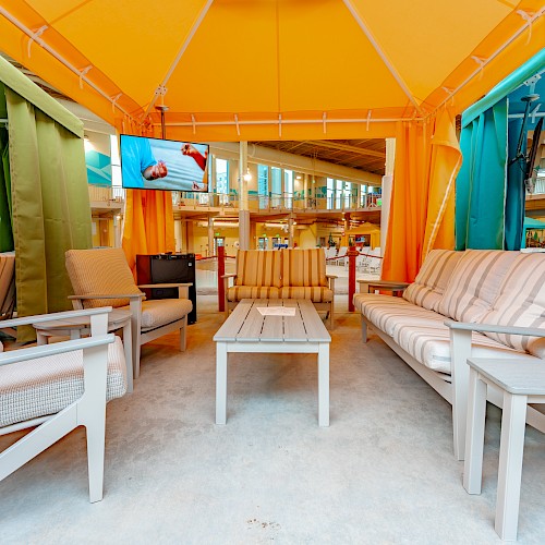 The image shows a cabana with patio furniture, a TV, and colorful curtains, creating a cozy and vibrant seating area.
