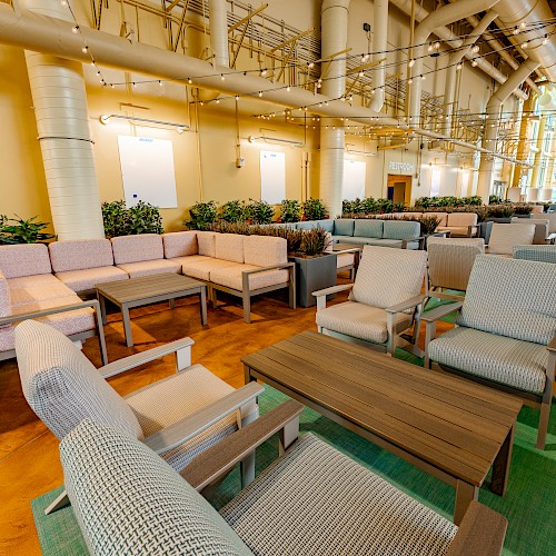 The image shows an indoor seating area with modern furniture, including sofas, chairs, and tables, set in a room with high ceilings.