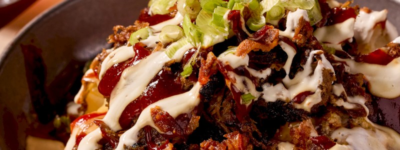 Meat Me Later - Choose one meat (pulled pork, smoked sausage, or chopped brisket) topped with butter, house rub, house-made queso, white cheddar cheese, green onion, candied bacon, sour cream, and Smokestack BBQ sauce