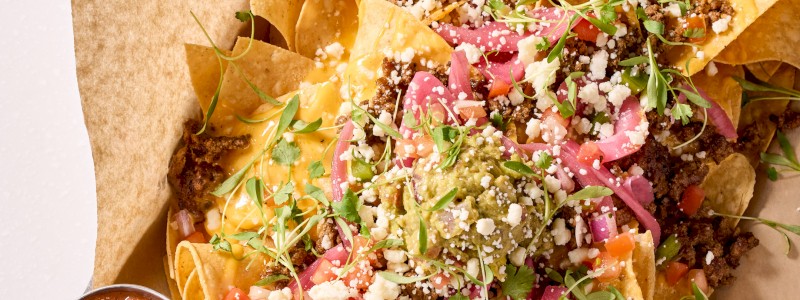 BASES LOADED NACHOS - GF. Cheddar cheese, seasoned ground beef, pickled
red onions, pico de gallo, guacamole, queso fresco,
micro cilantro, and fresh chipotle salsa.