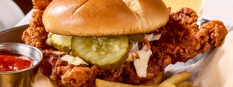 NASHVILLE HOT HONEY CHICKEN SANDWICH - Crispy chicken, hot honey drizzle, coleslaw, lettuce,
and tomato on a brioche bun.